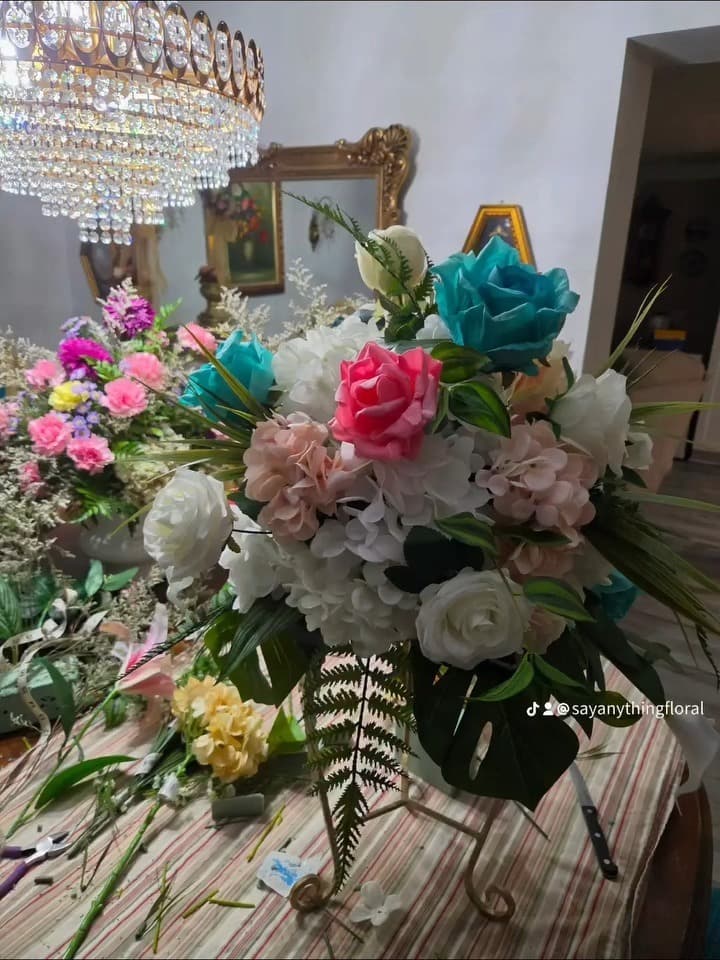Jewel-toned silk centerpiece with teal roses, fuchsia roses, blush hydrangea and white peonies beneath a crystal chandelier